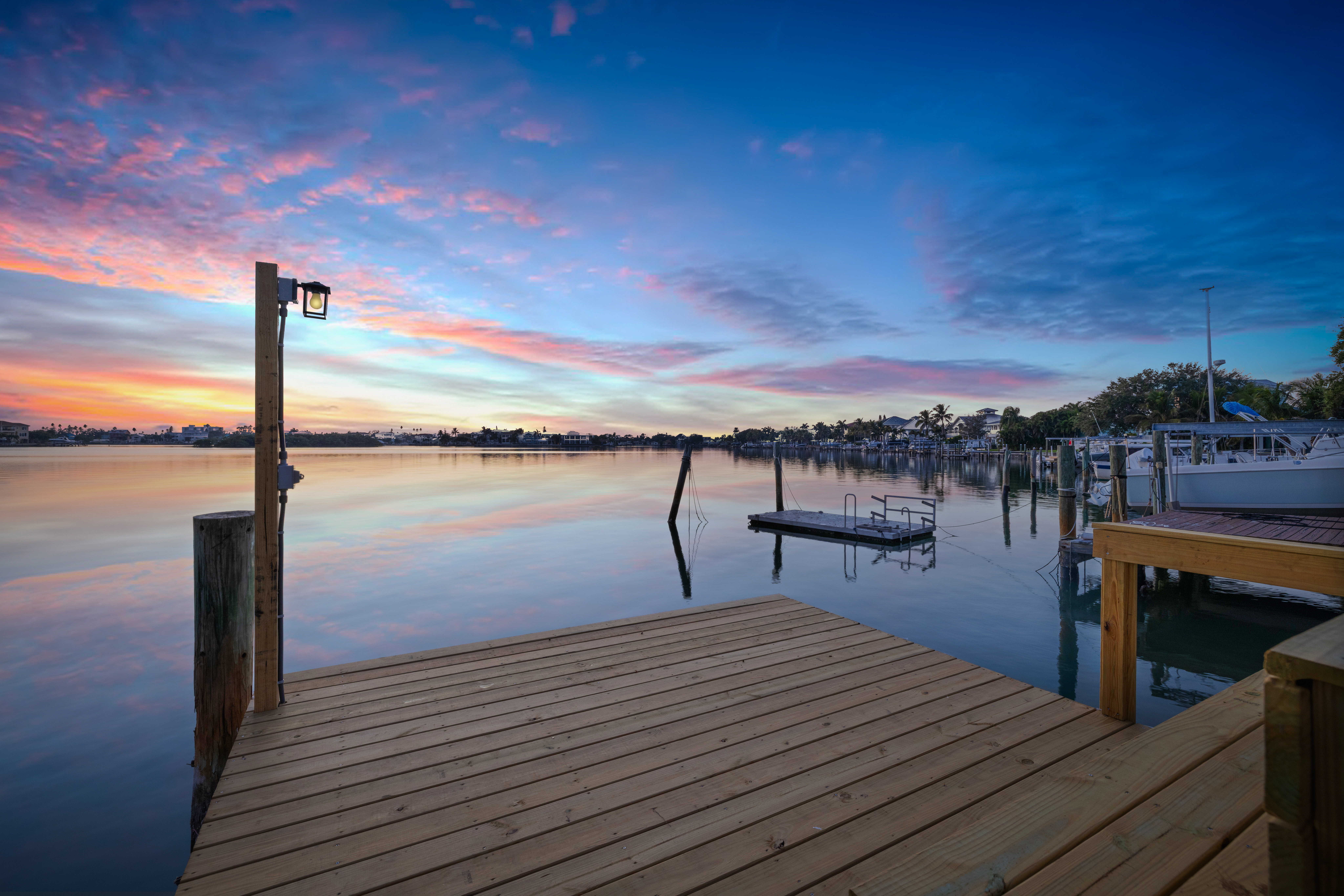 Sunset view from private dock of Intracoastal waterfront short-term rental investment property in Indian Rocks Beach Florida showing calm water pink and blue sky reflections and neighboring marina - waterfront dock access drives premium nightly rates in IRB STR market