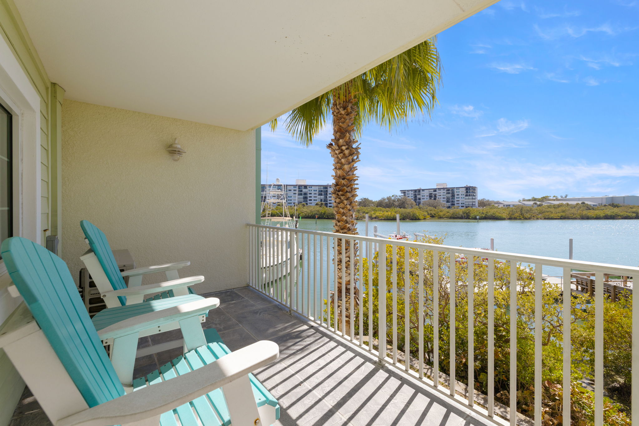 Balcony of Indian Rocks Beach Intracoastal waterfront condo with teal Adirondack chairs palm tree and direct Intracoastal Waterway views - waterfront balcony views drive premium nightly rates and five star guest reviews in the IRB STR condo market