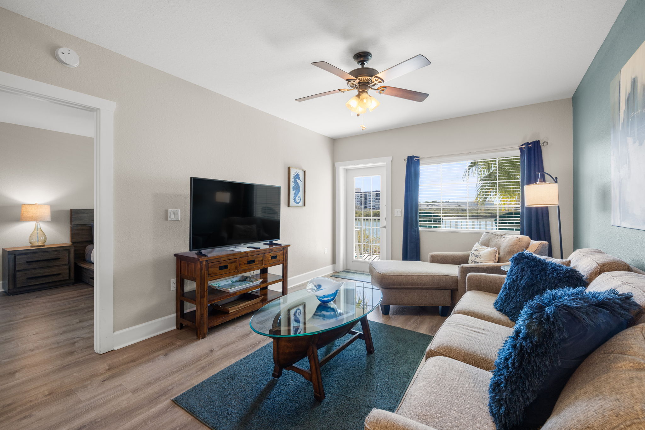 Turnkey furnished living room in Indian Rocks Beach Intracoastal waterfront condo with sectional sofa coastal decor flat screen TV and balcony access - fully furnished STR condo interior ready for immediate guest bookings