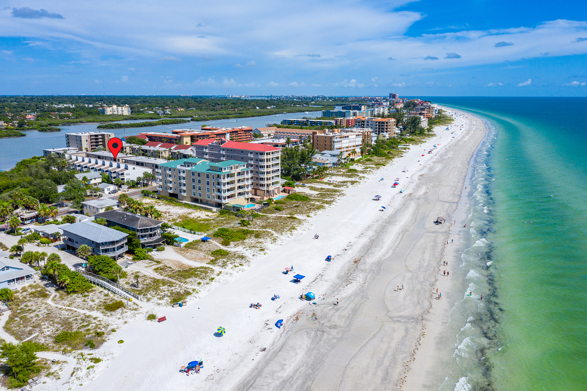 Aerial view looking south along Indian Shores Florida barrier island showing condos on both sides of Gulf Boulevard Gulf of Mexico on the right Intracoastal Waterway on the left wide white sand beach The Narrows short-term rental investment properties Pinellas County