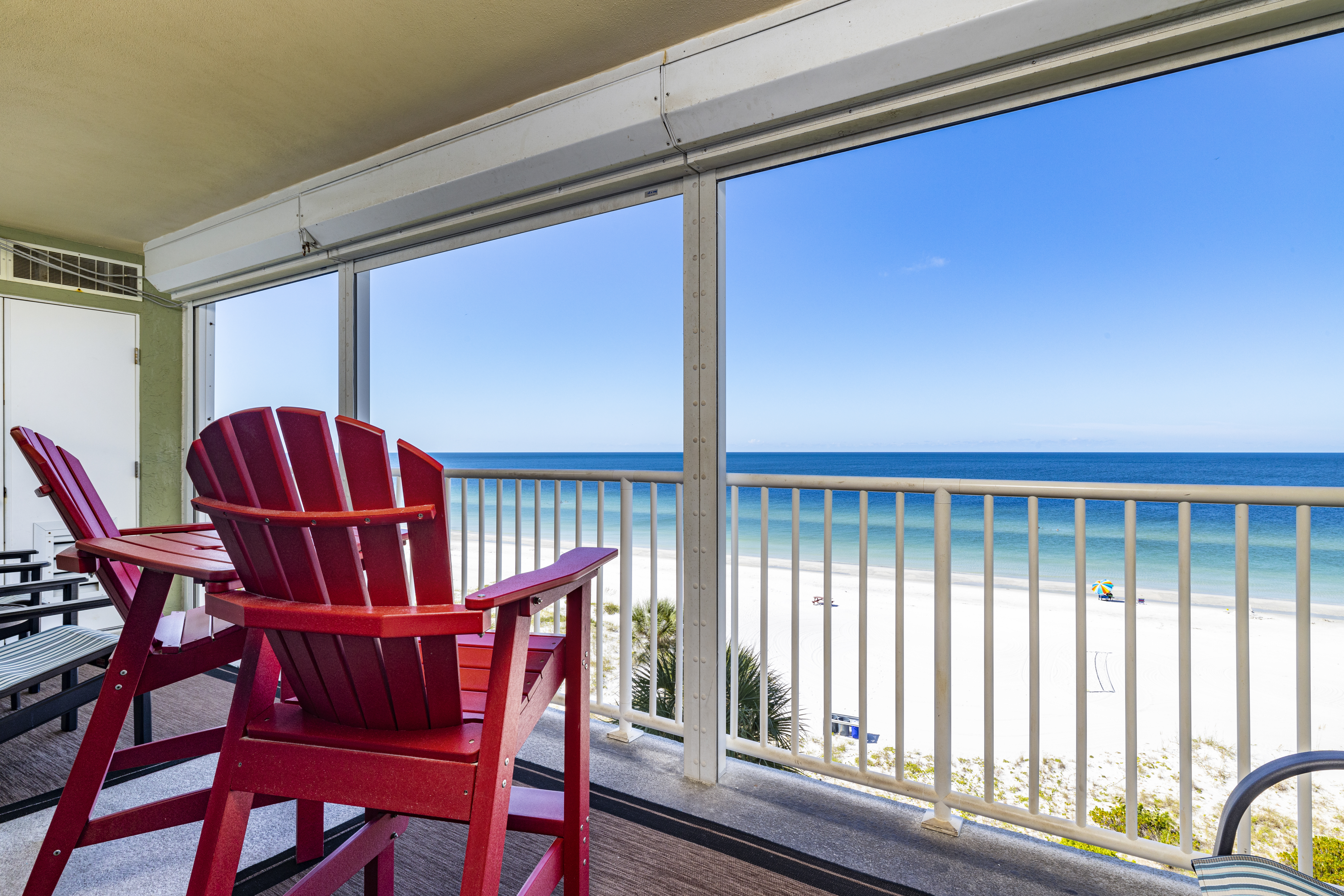 Gulf-front vacation rental condo balcony in Indian Shores Florida with red Adirondack chairs looking out at white sand beach and Gulf of Mexico Pinellas County short-term rental investment