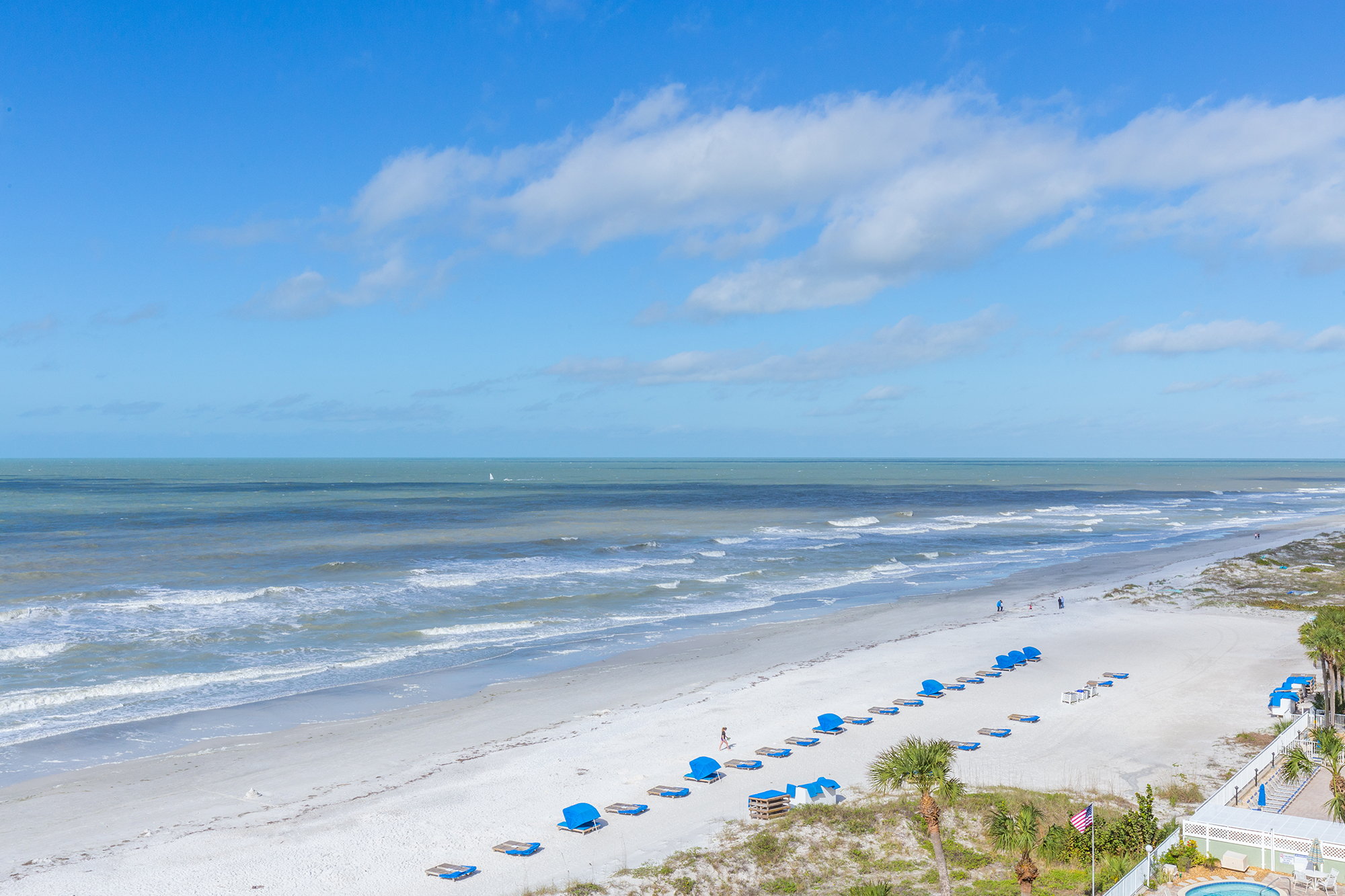 Gulf of Mexico view from elevated Indian Shores Florida vacation rental condo balcony showing white sand beach with rows of blue beach chairs palm trees and open water short-term rental investment property Pinellas County Gulf Beaches