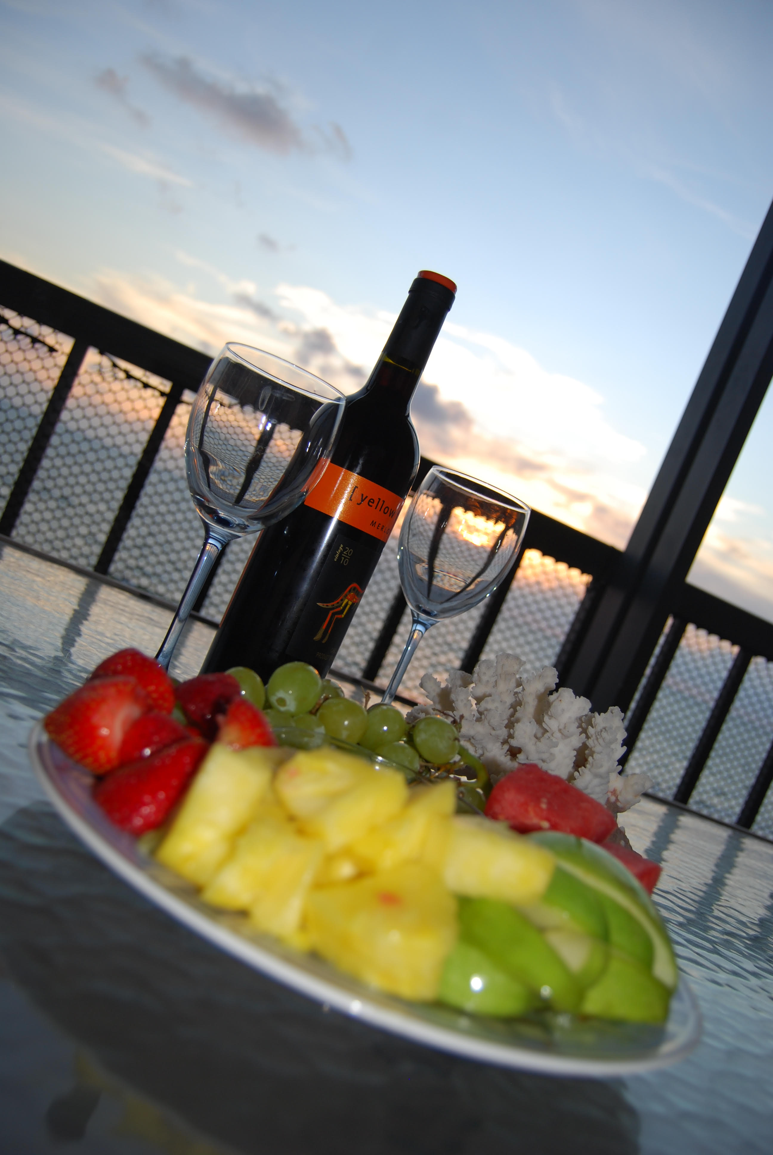 Gulf of Mexico sunset view from screened balcony of Indian Shores Florida Gulf-front vacation rental condo in 2011 with fruit platter strawberries pineapple grapes and wine glasses on balcony table short-term rental investment property Pinellas County