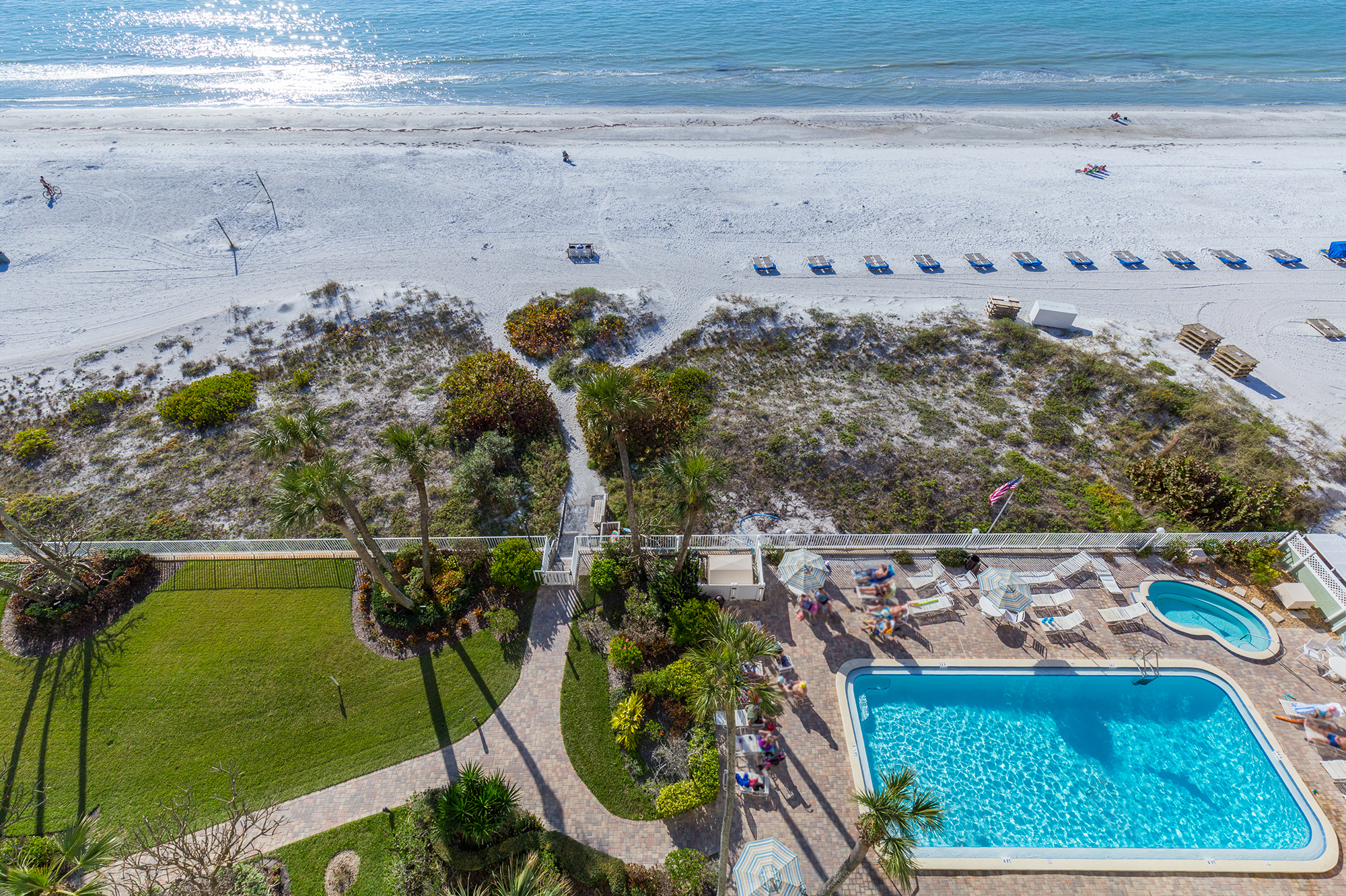 Overhead aerial view of Sand Castle 1 pool deck and beach access path in Indian Shores Florida showing pool chairs white sand beach and Gulf of Mexico Gulf-front vacation rental condo investment Pinellas County