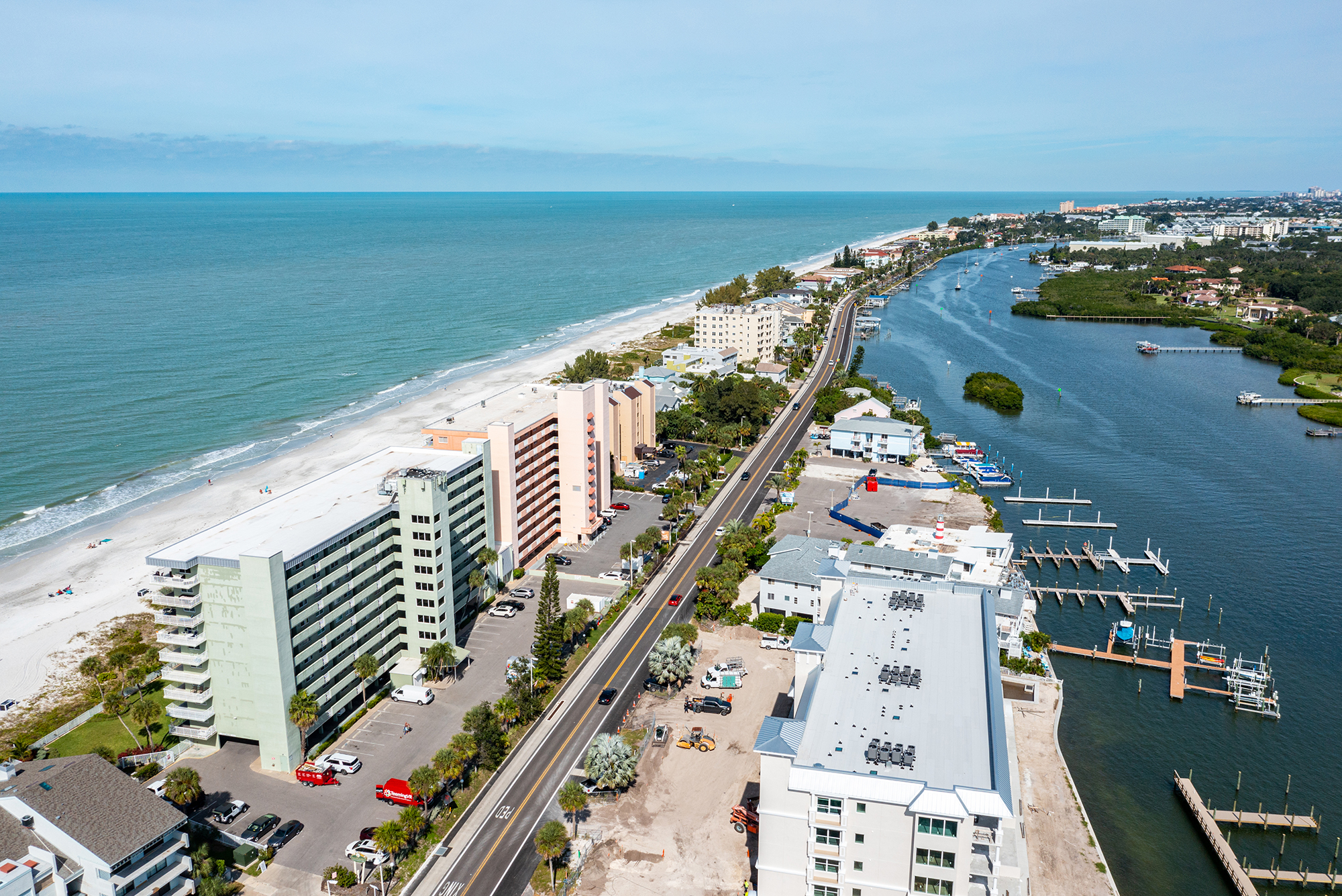 Aerial view looking north along Indian Shores Florida barrier island showing The Narrows with Gulf of Mexico white sand beach on the left Gulf Boulevard two-lane road in the center and Intracoastal Waterway with boat docks on the right short-term rental investment properties Pinellas County