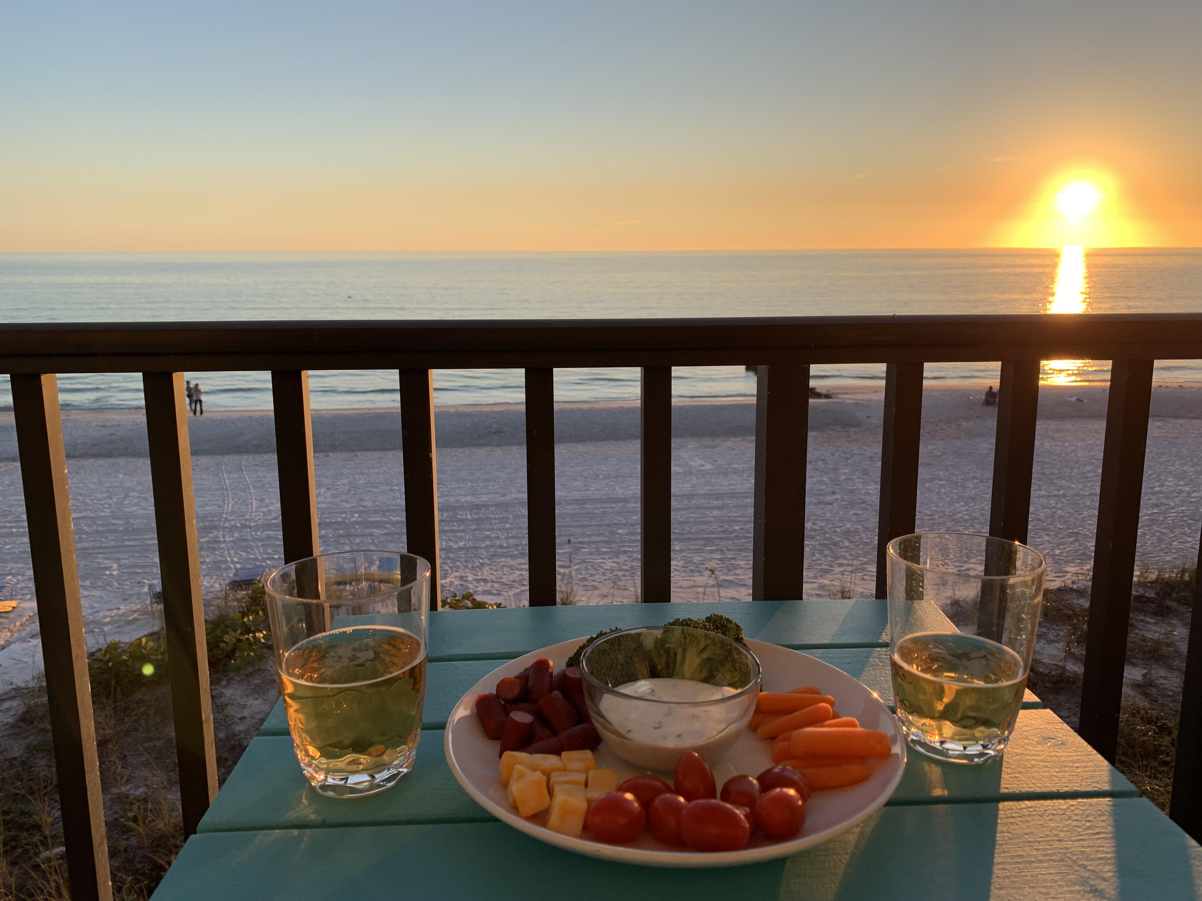 Gulf front condo balcony sunset view with dinner and wine overlooking white sand beach and Gulf of Mexico in Madeira Beach Florida - short-term rental vacation income property Pinellas County