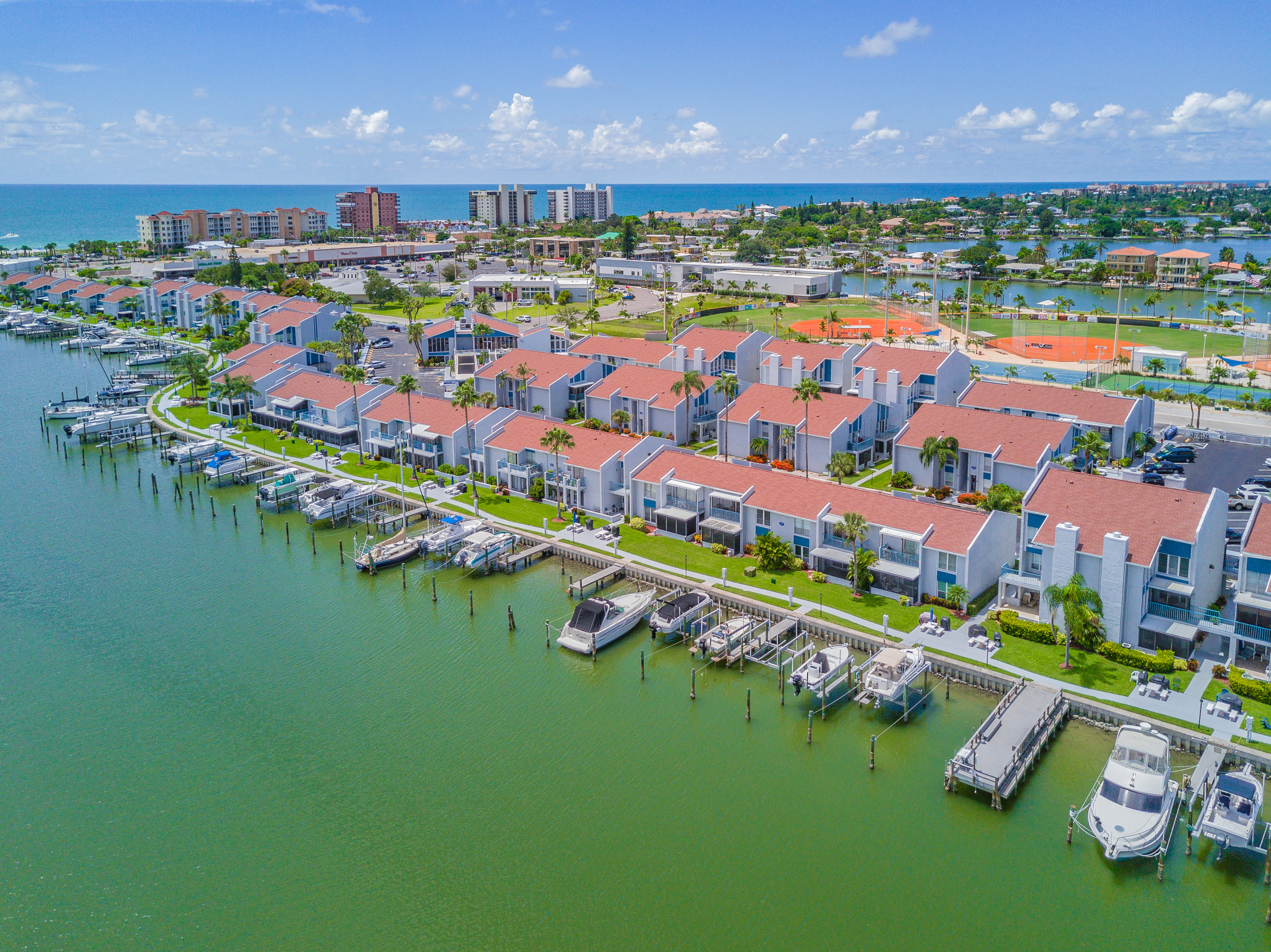 Aerial view of Madeira Beach Yacht Club condos with private boat docks and R.O.C. Park baseball fields showing bay-side short-term rental community Pinellas County Florida