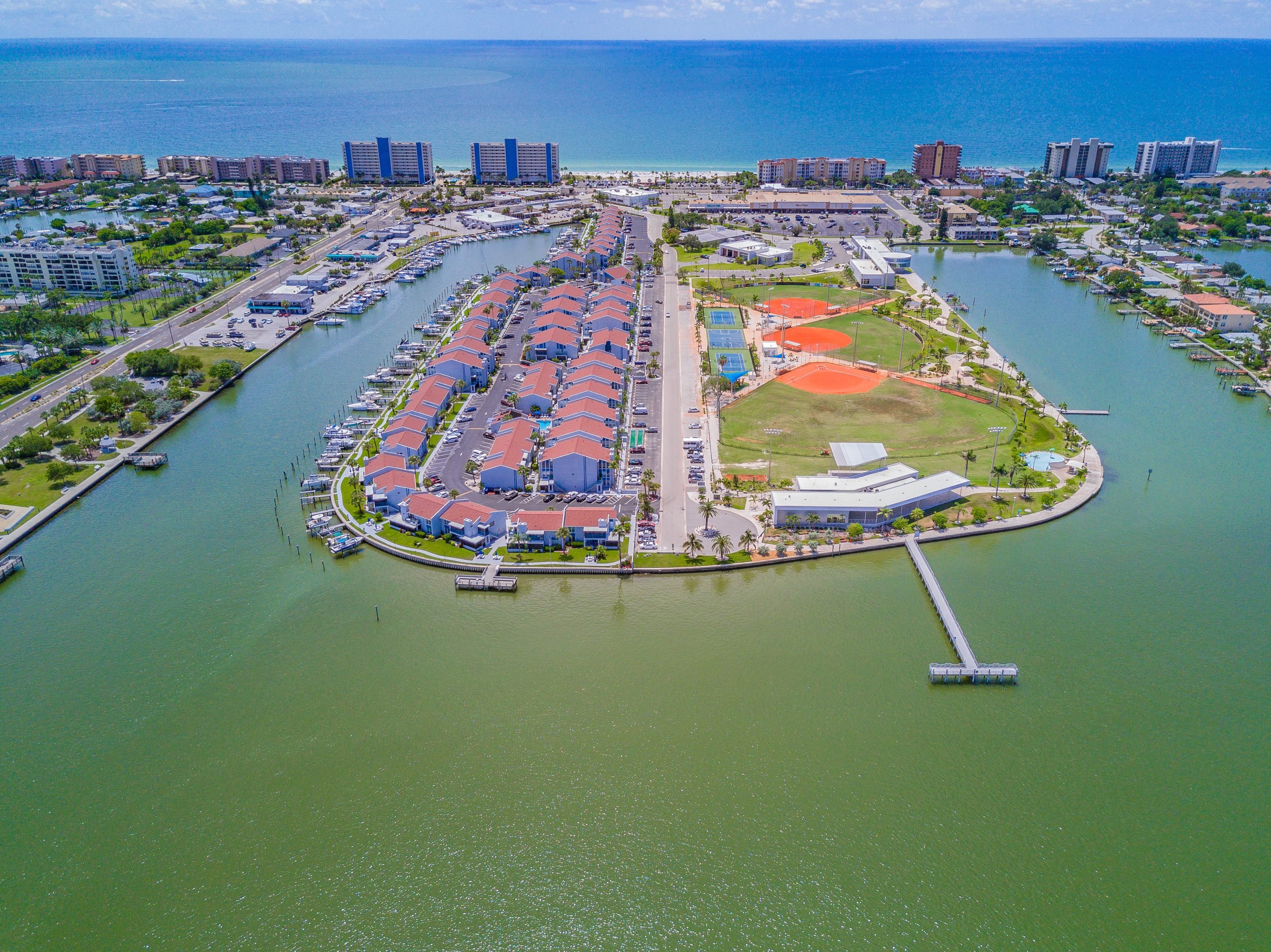 Aerial view of Madeira Beach Yacht Club condos with boat slips R.O.C. Park softball fields and Tom Stuart Causeway connecting barrier island to Pinellas County mainland Florida