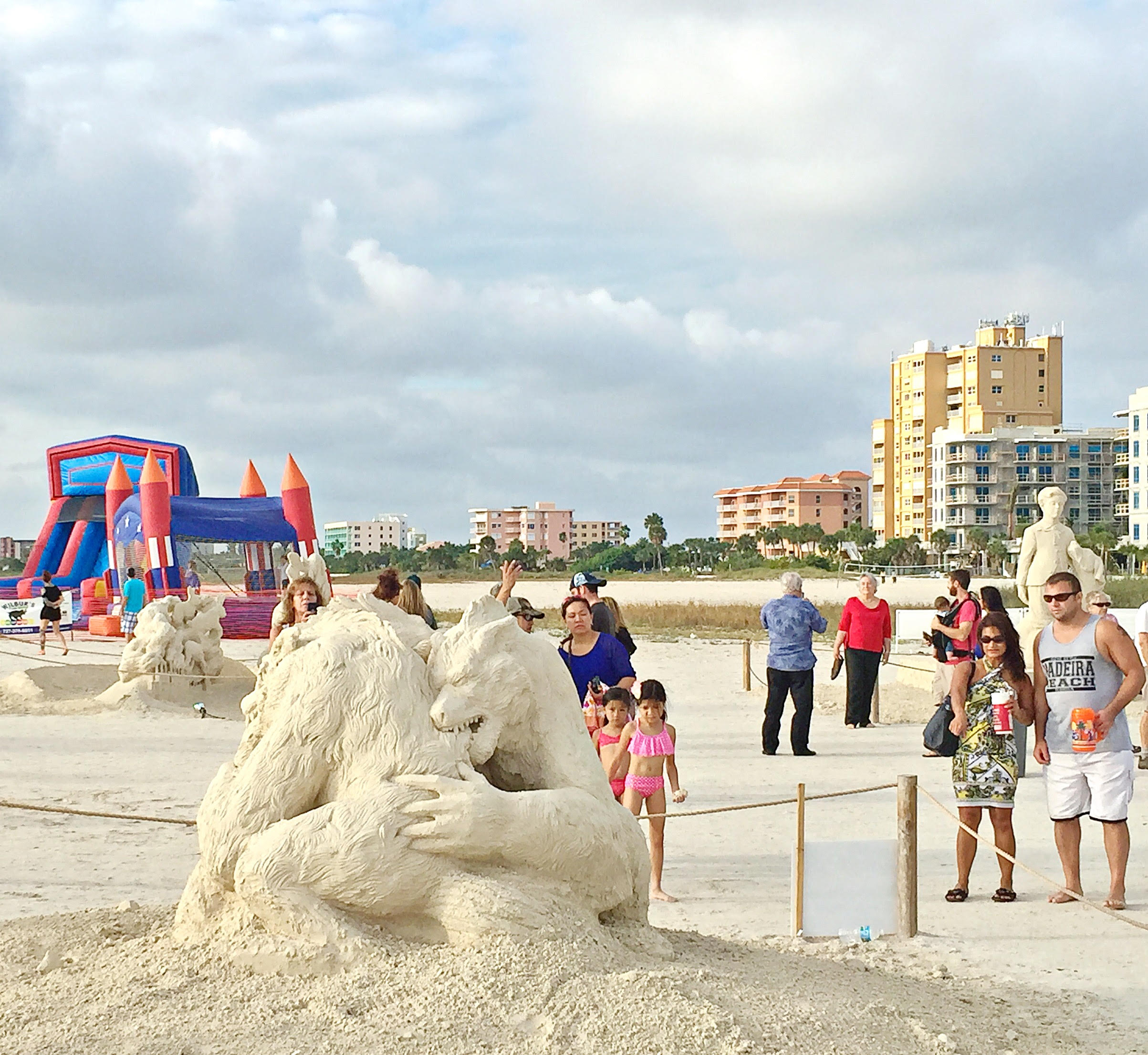Crowds walking among international sand sculptures at Sanding Ovations competition on Treasure Island Beach Florida with Gulf Boulevard vacation rental condo buildings in background Pinellas County