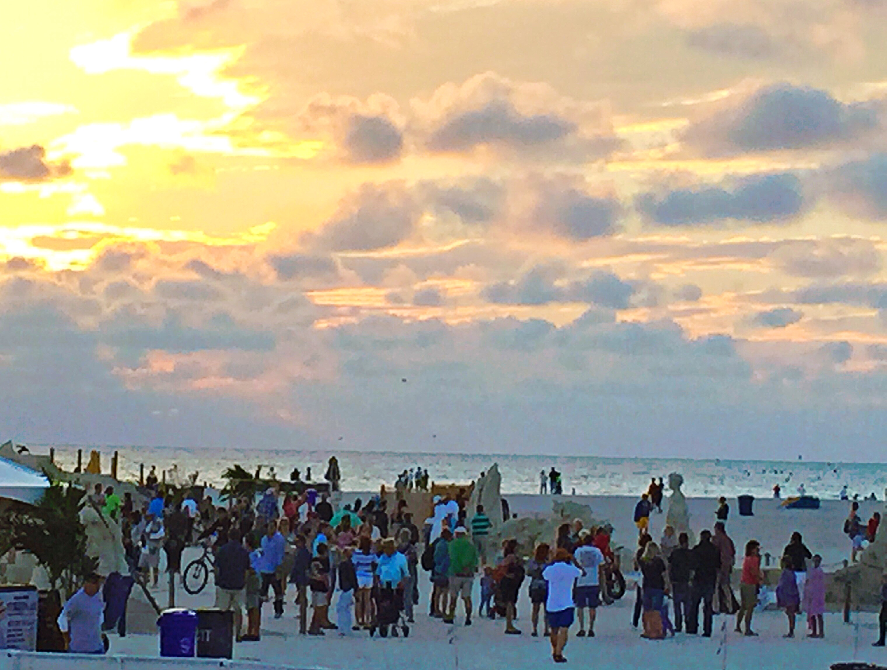 Large crowd gathered at Sanding Ovations international sand sculpting competition at sunset on Treasure Island Beach Florida with Gulf of Mexico in background and sand sculptures visible , annual November event drives short-term rental demand on the Pinellas Gulf Beaches